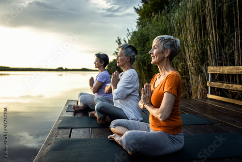 Group of senior woman doing yoga exercises by the lake.