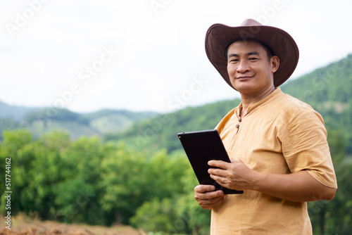Fototapeta Portrait of Asian handsome naturalist is at forest, wears hat, holds smart tablet