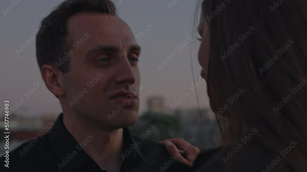 A man in a dark suit dances with a woman in a bright red dress with a slit on the leg. Rooftop patio area, slow dance setting sun. Romantic evening married couple love. Date surprise rooftop city view A man in a dark suit dances with a woman in a bright red dress with a slit on the leg. Rooftop patio area, slow dance setting sun. Romantic evening married couple love. Date surprise rooftop city view