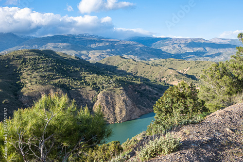 Fototapeta Naklejka Na Ścianę i Meble -  Breath-taking view from the top on green lake surrounded by picturesque mountain alley with trees and bushes in sunny summer day with blue sky and white clouds in background.