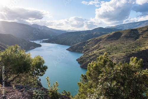 Fototapeta Naklejka Na Ścianę i Meble -  Breath-taking view from the top on green lake surrounded by picturesque mountain alley with trees and bushes in sunny summer day with blue sky and white clouds in background in Spain Andalusia