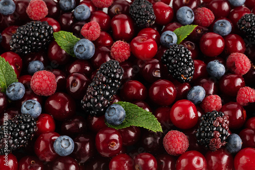 Bright fruit and berry background of cherries, raspberries, blueberries, blackberries and mint leaves.