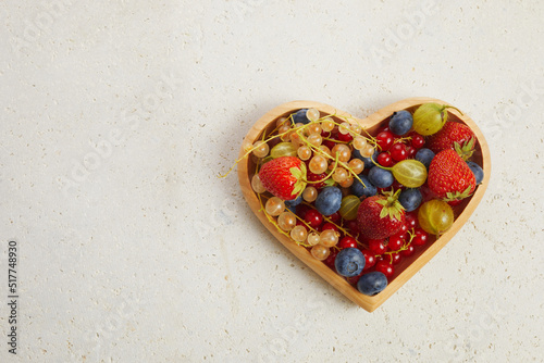 Berries mix in in a heart shaped bowl on travertine background