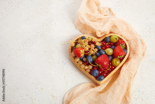 Berries mix in in a heart shaped bowl on travertine background