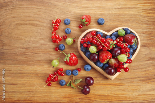 Berries mix in in a heart shaped bowl spilled on rustic wooden table