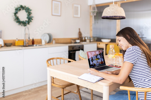 Young adult woman using laptop computer while having a video call with multiracial team employees working from home office - Virtual meeting conference concept