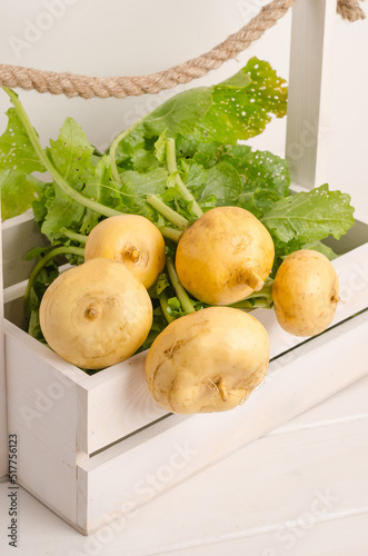 Fresh yellow turnip with stems and green leaves in a box on a white wooden background