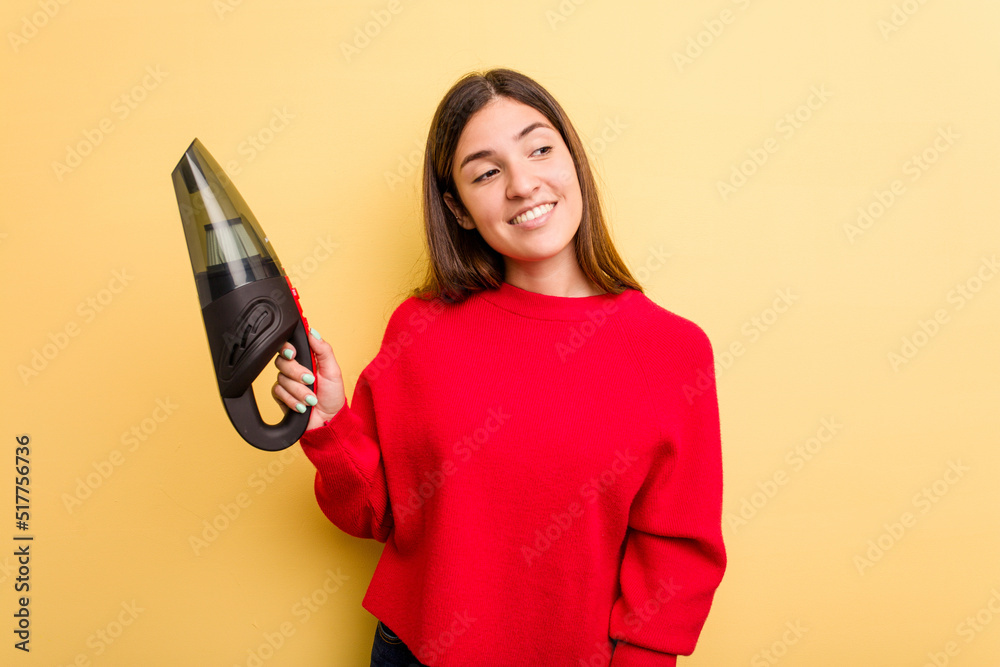 Young caucasian woman holding a hand vacuum cleaner isolated on yellow background looks aside smiling, cheerful and pleasant. Young caucasian woman holding a hand vacuum cleaner isolated on yellow background looks aside smiling, cheerful and pleasant.