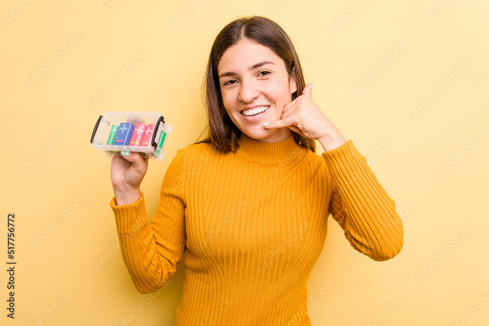Young caucasian woman holding a batteries box isolated on yellow background showing a mobile phone call gesture with fingers. Young caucasian woman holding a batteries box isolated on yellow background showing a mobile phone call gesture with fingers.