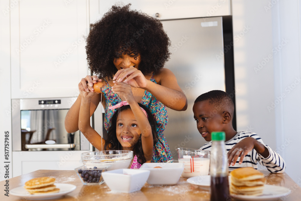 Multiracial mother with afro hair breaking egg with daughter in bowl while making breakfast on table Multiracial mother with afro hair breaking egg with daughter in bowl while making breakfast on table