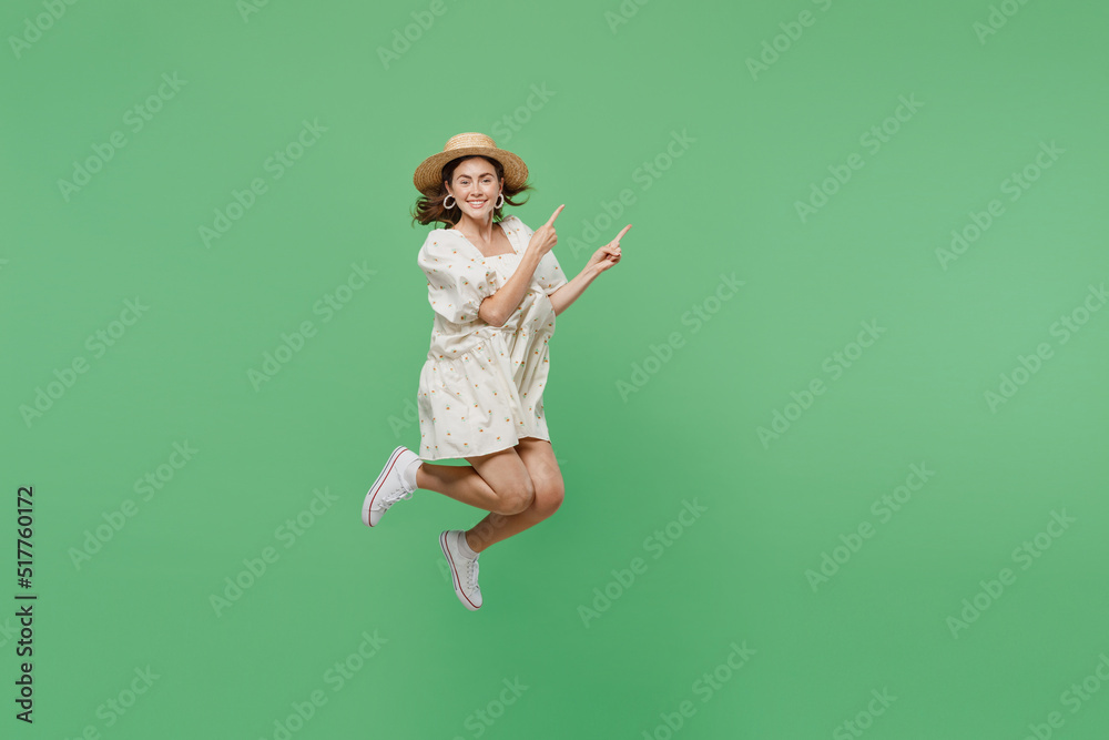 Full body young happy smiling overjoyed excited woman she 20s in white dress hat jump high point index finger aside on workspace area isolated on plain pastel light green background studio portrait.