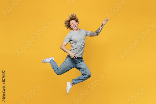 Full body rocker singer musician cool young caucasian man 20s he wear grey t-shirt jump high play guitar hand arm gesture isolated on plain yellow backround studio portrait. People lifestyle concept.