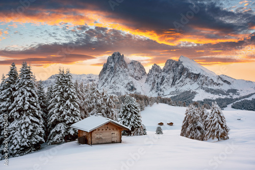 Picturesque landscape with small wooden log cabin on meadow Alpe di Siusi on sunrise time. Seiser Alm, Dolomites, Italy. Snowy hills with orange larch and Sassolungo and Langkofel mountains group © Ivan Kmit