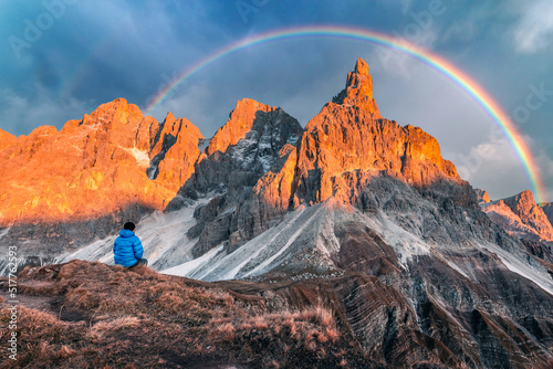 Tourist in Dolomite Alps. Pale di San Martino mountain group in sunset time. Hight mountains with glacier glowing by sunset light with rainbow. San Martino di Castrozza, Dolomites, Trentino, Italy photo