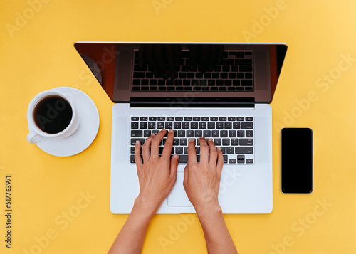 Freelancer at work. Top view photo. Woman is typing text at laptop on yellow desk. 