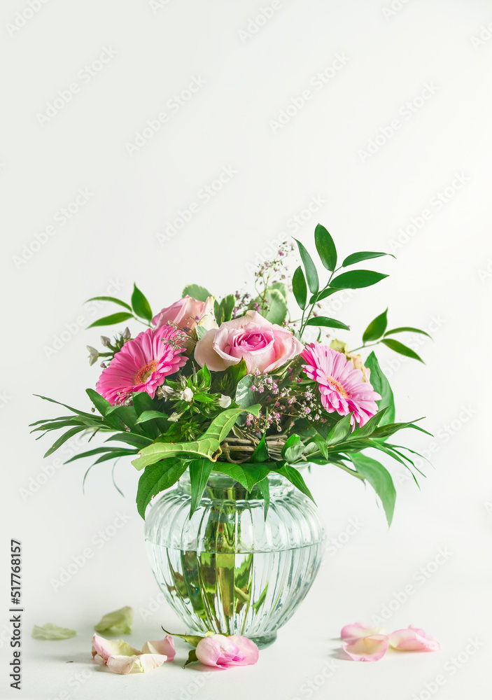 Obraz premium Beautiful summer flowers bouquet with roses and gerbera flower and green leaves in glass vase at white background. Front view.