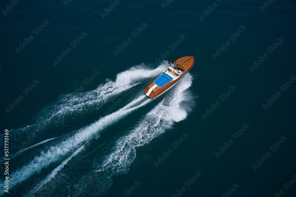 Wooden boat for millionaires movement on the water top view. Man and woman travel on a boat aerial view. Expensive wooden boat in a modern design fast movement on dark blue water aerial view.