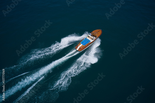 Wooden boat for millionaires movement on the water top view. Man and woman travel on a boat aerial view. Expensive wooden boat in a modern design fast movement on dark blue water aerial view. © Berg