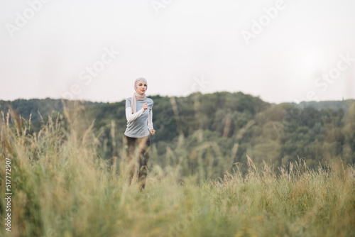 Happy arabian woman in hijab in activewear running at summer park. Young woman spending free time activity on fresh air. Smiling muslim female jogging during outdoors workout. © sofiko14