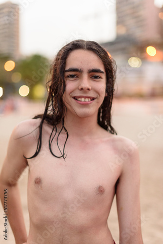 teenager with long hair, after bathing on a city beach with the buildings and lights in the background out of focus.