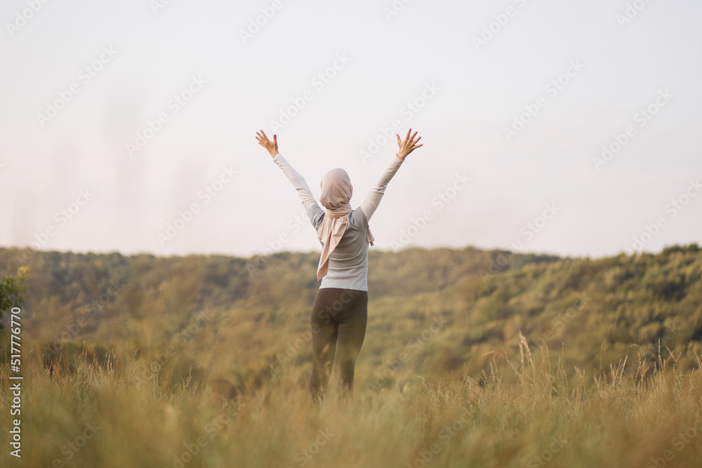Arabian young woman is practicing yoga in the summer park. A Muslim woman is looking aside exercising outdoor and breathing fresh air outstretching arms . Fit arabic woman training in a park Arabian young woman is practicing yoga in the summer park. A Muslim woman is looking aside exercising outdoor and breathing fresh air outstretching arms . Fit arabic woman training in a park