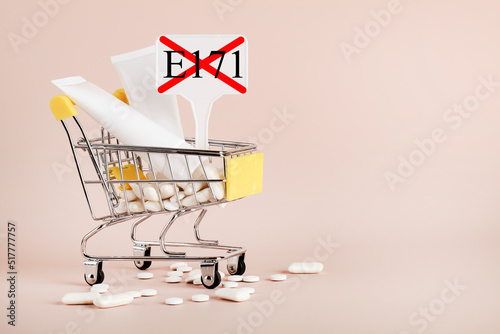 Titanium dioxide, E171, dangerous additive concept. gum, pills, toothpaste, cream in basket and sign with E171 on beige background. copy space photo