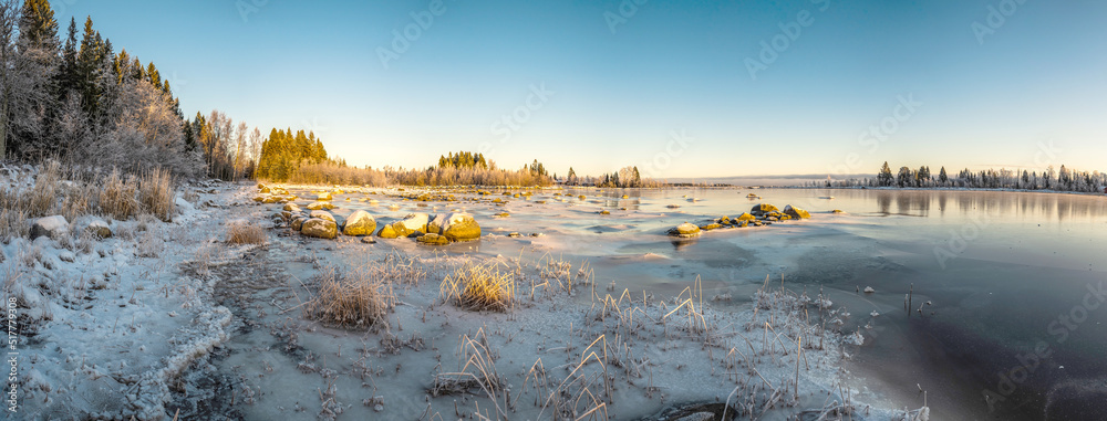 A poanoramic winter sunny landscape of frozen seashore in a chilly weather with clear sky and frozen stone
