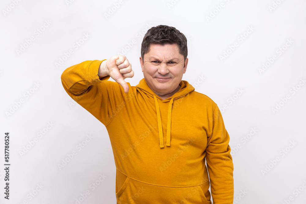 Middle aged man showing thumbs down, expressing disapproval, criticizing and disagreeing with suggestion, wearing urban style hoodie. Indoor studio shot isolated on white background. Middle aged man showing thumbs down, expressing disapproval, criticizing and disagreeing with suggestion, wearing urban style hoodie. Indoor studio shot isolated on white background.