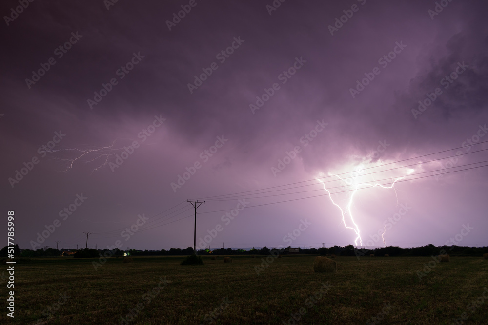 Thunderstorm above field with roll bales of hay at night, cloud to ground branched lightning, lightning in clouds at night in countryside Thunderstorm above field with roll bales of hay at night, cloud to ground branched lightning, lightning in clouds at night in countryside