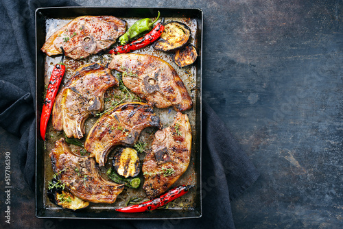 Barbecued lamb saddle back chop steaks with chili and eggplants served as top view on a rustic metal sheet with copy space right