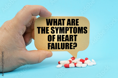 On a blue surface are pills in a persons hand, a sign with the inscription - What are the symptoms of heart failure photo