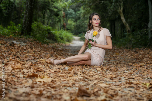 A Young Woman Smilling And Holding A Yellow Rose Sitting In The Forest