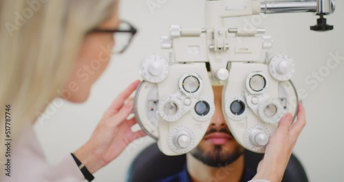 Optometrist using eye phoropter machine to examine patients refractor strength in clinic consult. Healthcare medical professional adjusting ophthalmic equipment, checking for astigmatism or myopia photo