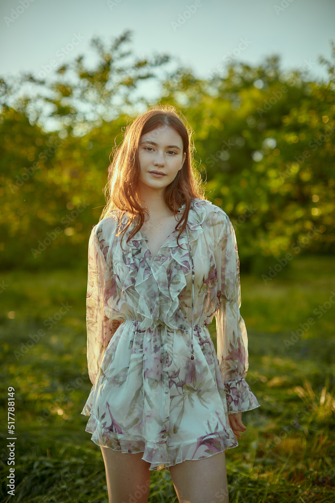 A young attractive woman in a light summer dress walks in the park.