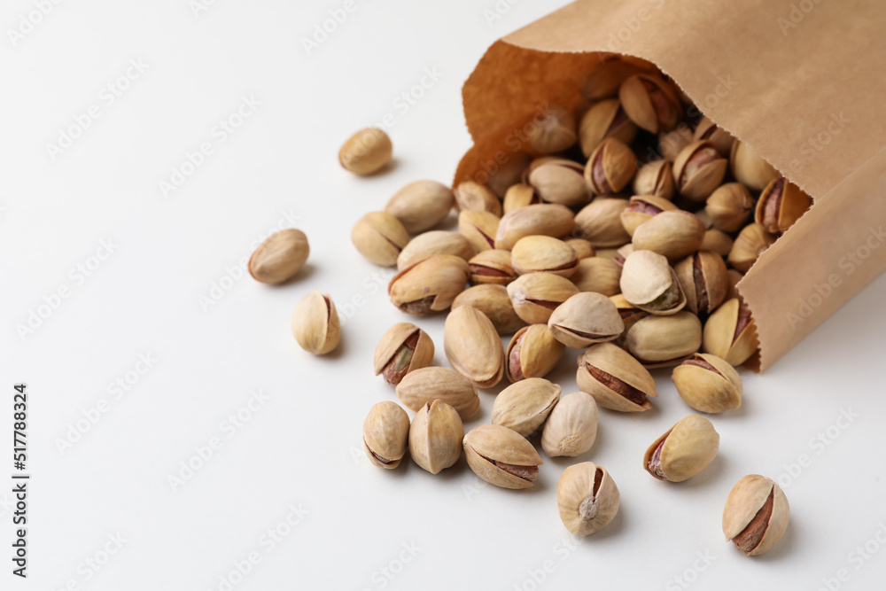 Overturned paper bag with pistachio nuts on white background, closeup. Space for text Overturned paper bag with pistachio nuts on white background, closeup. Space for text