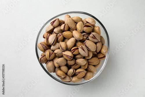 Bowl with pistachio nuts on white background, top view