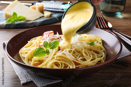 Cuadro en lienzo Pouring tasty cheese sauce onto spaghetti with meat on wooden table, closeup