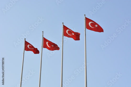 Four Turkish flags blowing in the wind on flagpoles against a blue cloudless cloud-free sky on a sunny day