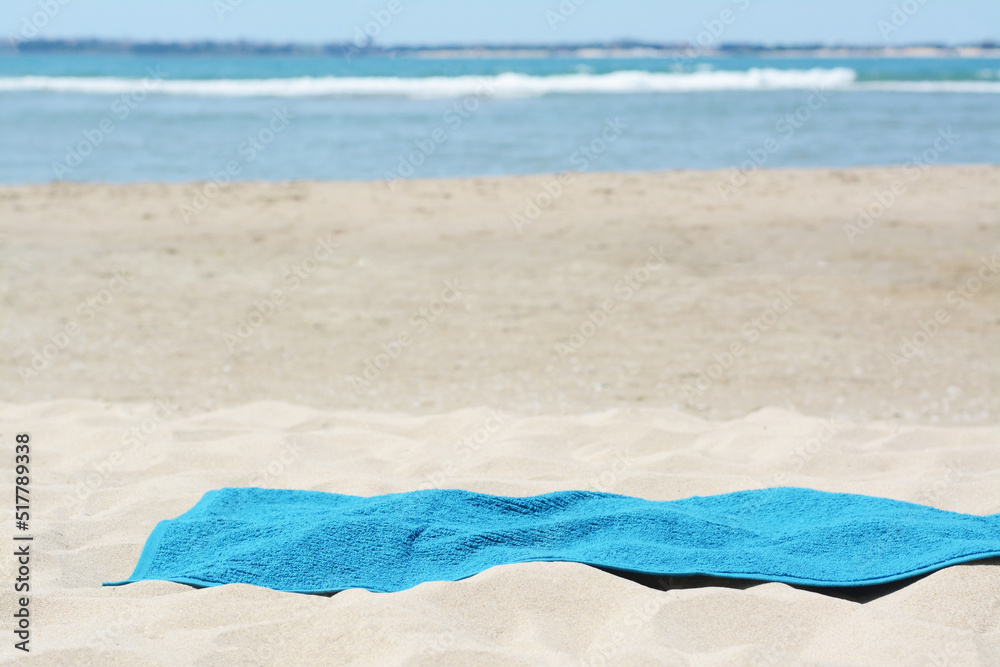 Fototapeta premium Soft blue towel on sandy beach near sea, space for text