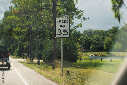 Photos Speed limit 35 mph sign, taken from the passenger side of a moving vehicle, driving on a rural forest road on a partly cloudy afternoon