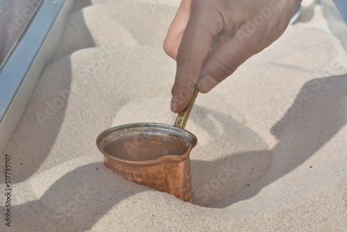 A hand holding a Turkish sand coffee copper cup in the sand