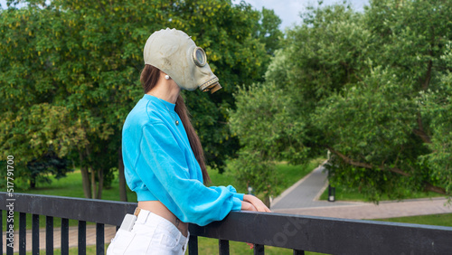 A girl in a gas mask stands on a bridge across the river. Alienation in the city. Fashion, ecology and loneliness concepts.