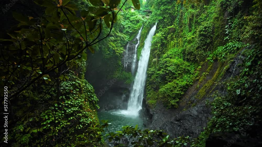 waterfall with rocks among tropical jungle with green plants and trees and water falling down