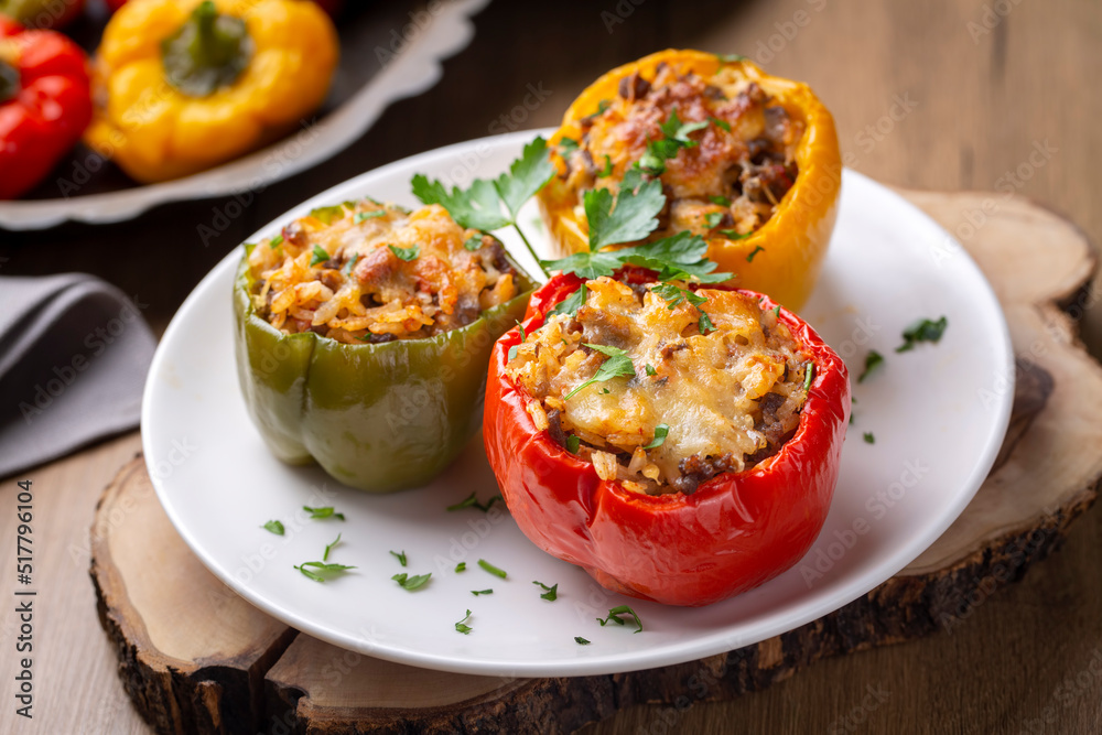 Stuffed peppers, halves of peppers stuffed with rice, dried tomatoes, herbs and cheese in a baking dish on a blue wooden table, top view. (Turkish name; biber dolmasi)