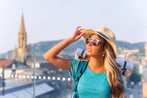 Young travel girl with backpack, sleeping bag, sunglasses and hat on vacation in the city