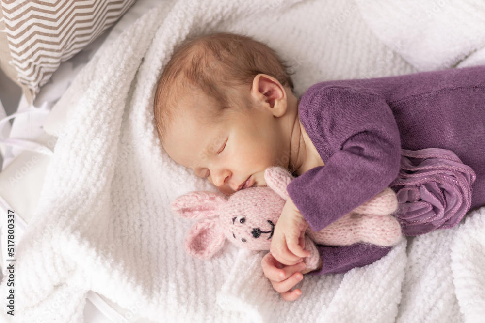 Cute newborn baby girl sleeps at home in her crib with her favorite toy, the first month of life