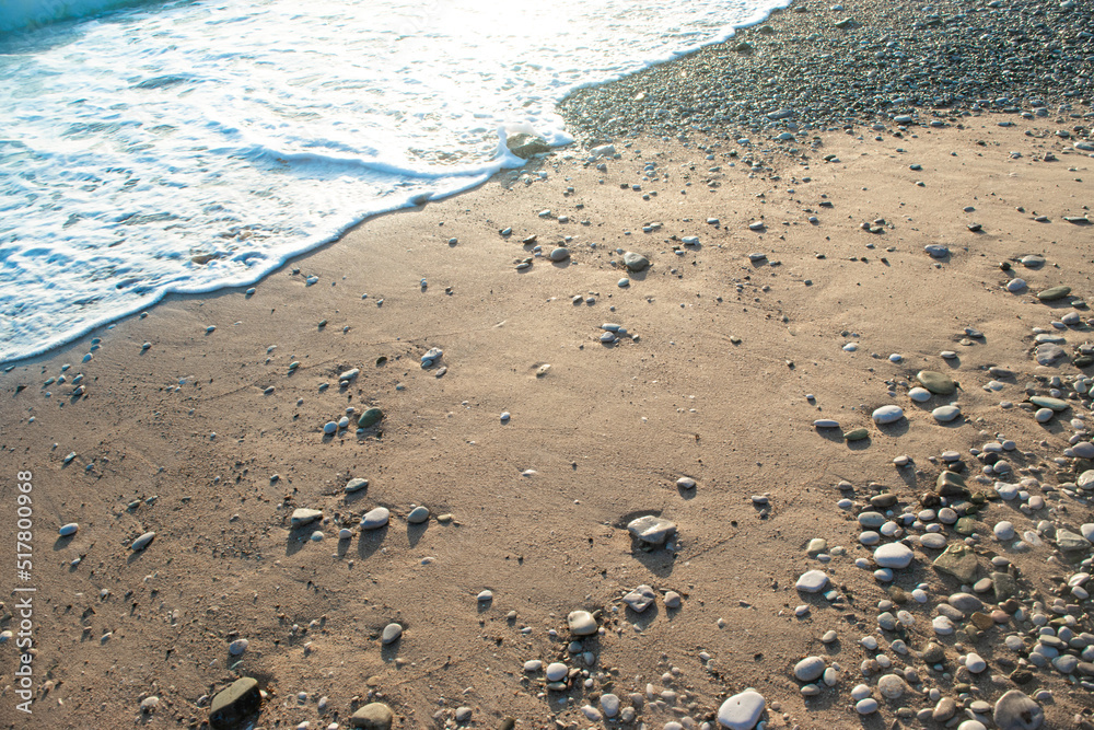 Sea foam surf, sand and pebbles on beach at setting sun rays. Sea foam surf, sand and pebbles on beach at setting sun rays.