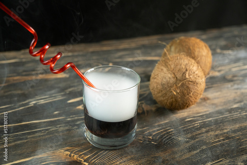 Smoky cockteil with brown liqueur. Whiskey drinks isolated on black backdrop. Close up view of a glass of whiskey on a black slate with a smoky background. Coconut smoky background. photo