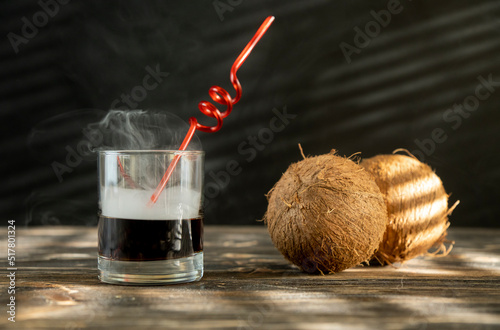 Smoky cockteil with brown liqueur. Whiskey drinks isolated on black backdrop. Close up view of a glass of whiskey on a black slate with a smoky background. Coconut smoky background. photo