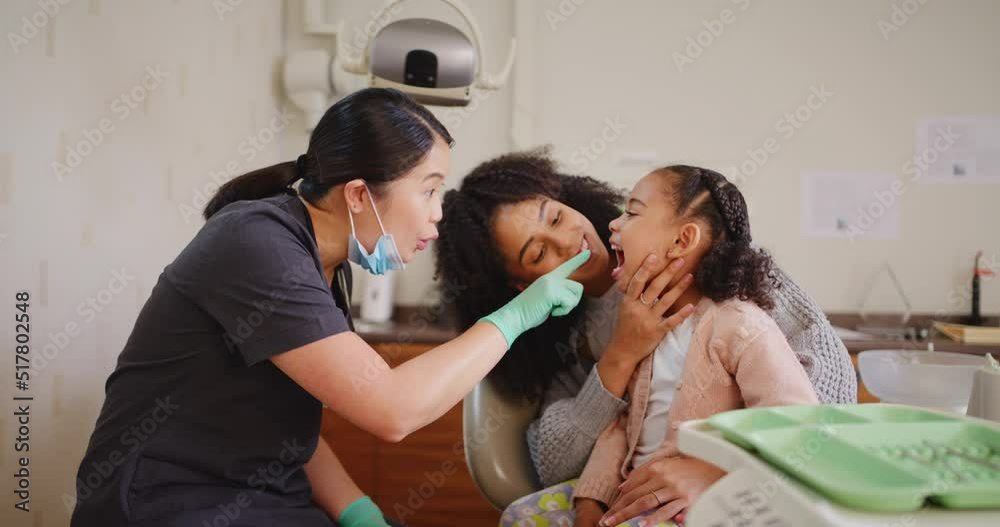 Dentist checking a young girls teeth during a checkup in a medical clinic. Brave little kid opening her mouth wide for an oral hygienist. Mother holding her child while consulting a dental expert Dentist checking a young girls teeth during a checkup in a medical clinic. Brave little kid opening her mouth wide for an oral hygienist. Mother holding her child while consulting a dental expert